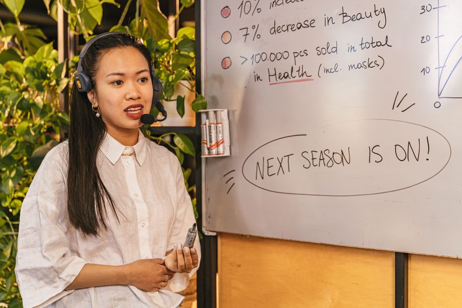 Woman presenting business statistics on whiteboard using headset, engaging audience
