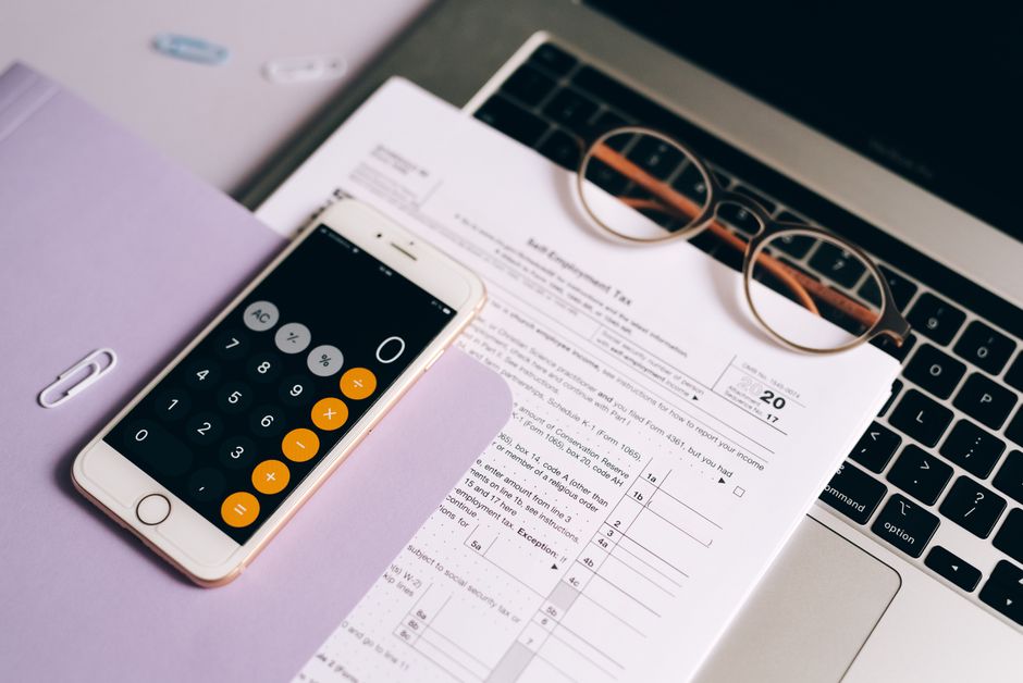 A smartphone with a calculator app on tax documents next to a laptop, emphasizing modern accounting