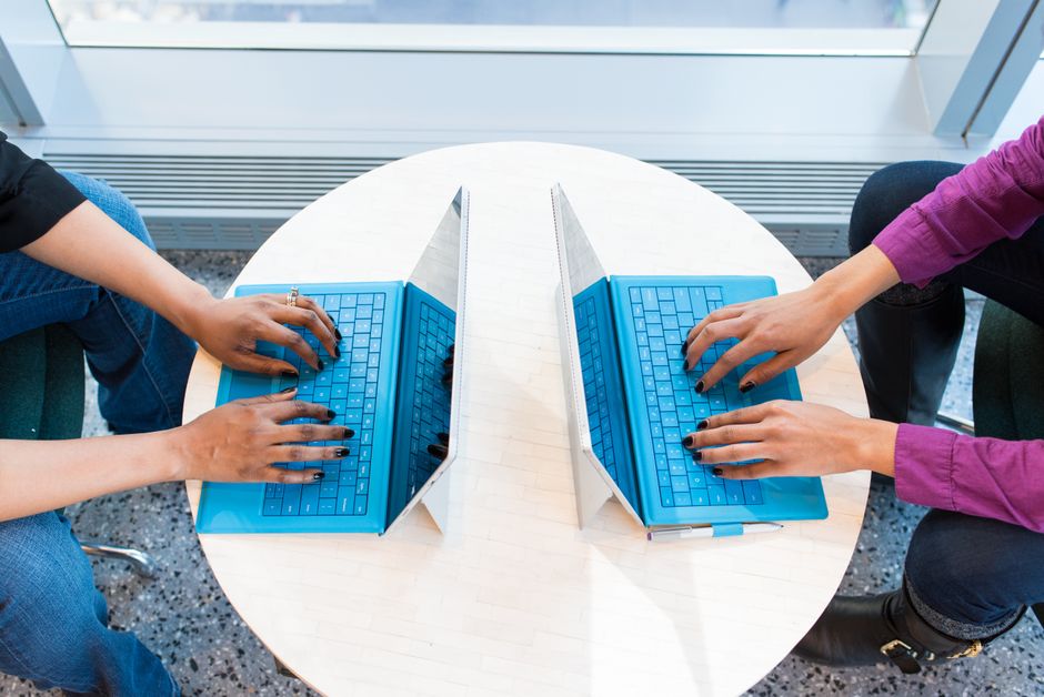 Two people working on blue laptops at a round table, focusing on teamwork and technology