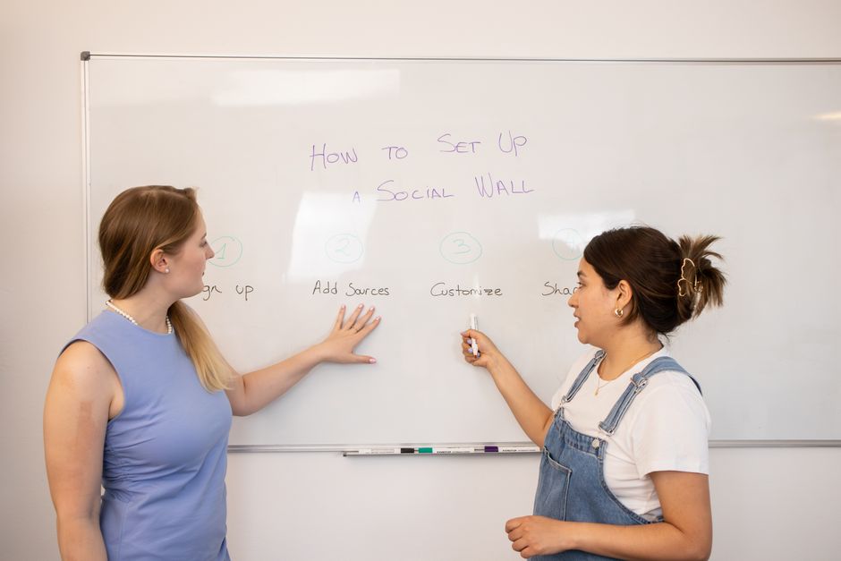 Two women preparing a social media wall on a whiteboard in an office setting
