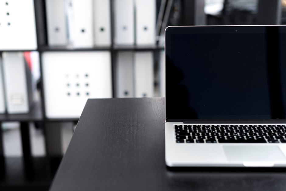 A sleek laptop on a desk in a modern office setting with organized shelves
