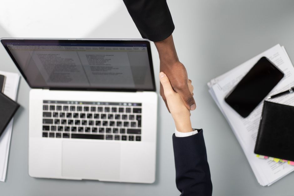 Overhead view of a professional handshake over a laptop, symbolizing business agreement
