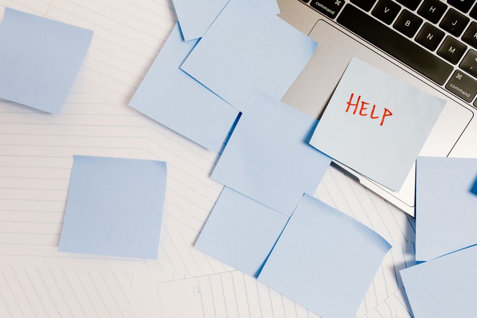 A cluttered workspace with sticky notes on a laptop, symbolizing overwhelm and need for help