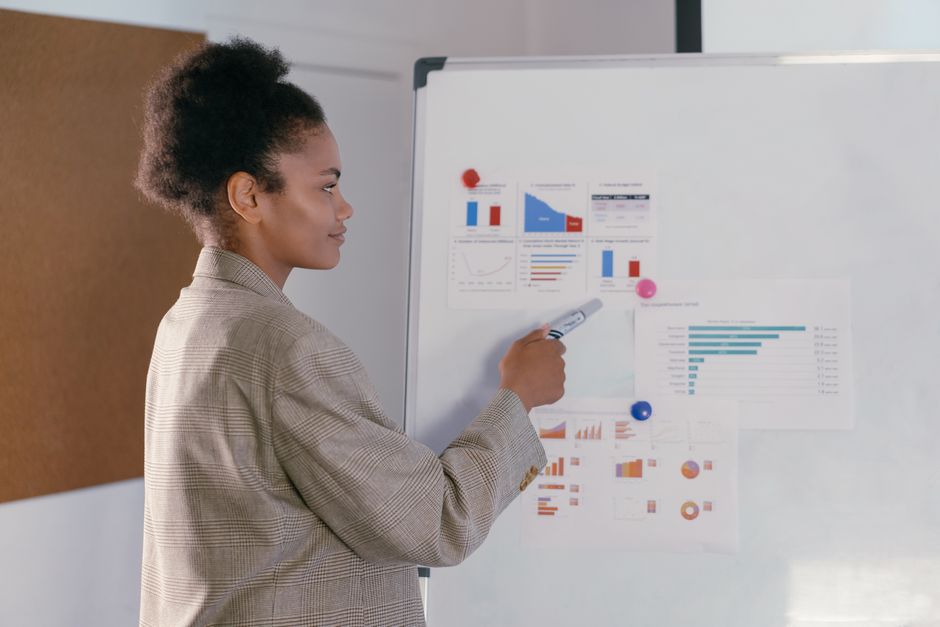 Professional woman in a blazer discusses finance graphs on a whiteboard during a presentation