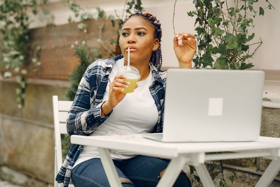 A young woman in a casual setting using a laptop and sipping a drink outdoors