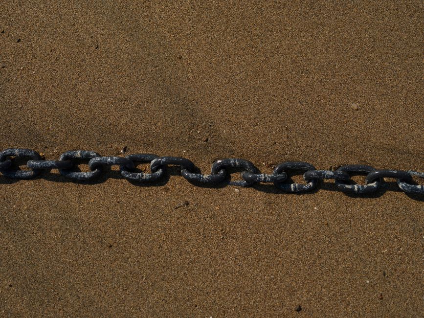 Close-up of a weathered chain lying on a sandy beach, showing maritime textures