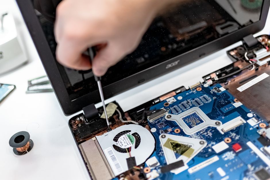Technician repairing a laptop motherboard, focusing on electronic components