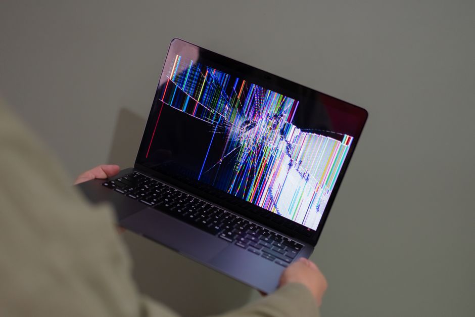 A broken laptop screen displayed with colorful glitch being held by a person