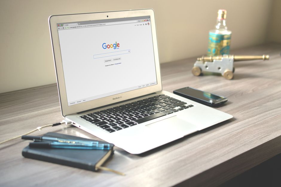 A neat workspace featuring a laptop displaying Google search, a smartphone, and a notebook on a wooden desk