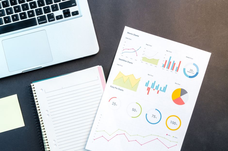 Flatlay of business report with colorful charts, a notebook, and a laptop for data analysis on a desk