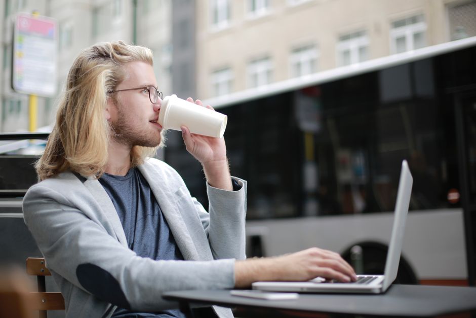Young man working remotely on laptop while enjoying a coffee outdoors