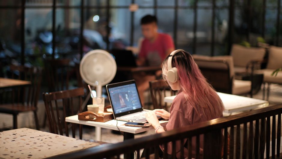 A woman with headphones edits a video on her laptop in a cozy café environment, Vietnam