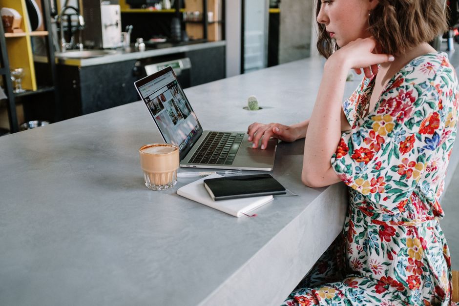 Young woman in a floral print dress working on a laptop in a modern café setting