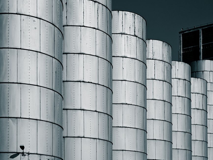 Close-up of industrial metal silos lined up against a dark blue sky, showcasing symmetry