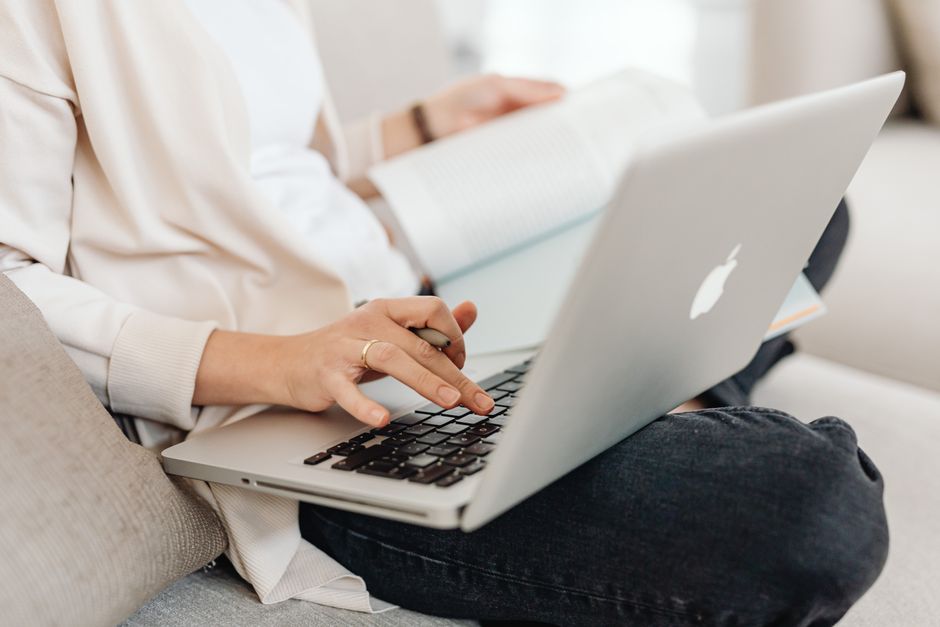 Close-up of a person multitasking, typing on a laptop while holding a book on their lap
