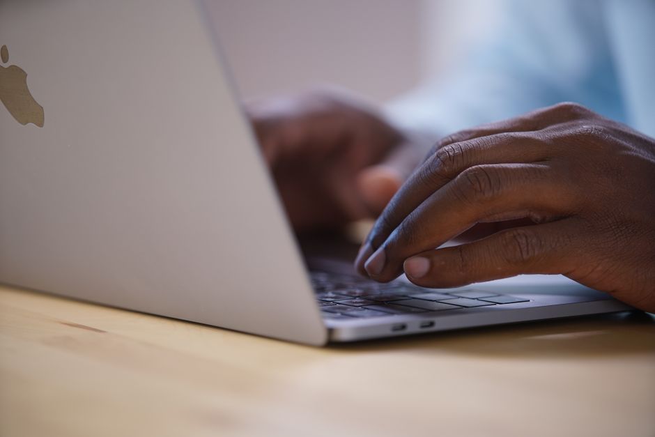 African American hands typing on a laptop keyboard on a wooden surface