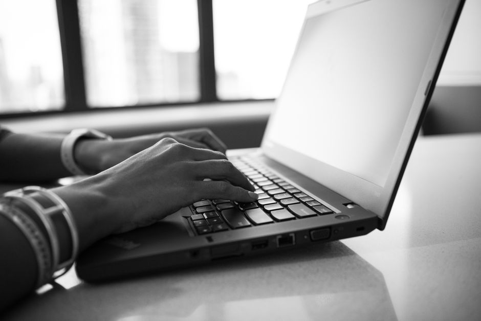 Close-up black and white photo showing hands typing on a laptop, emphasizing modern technology