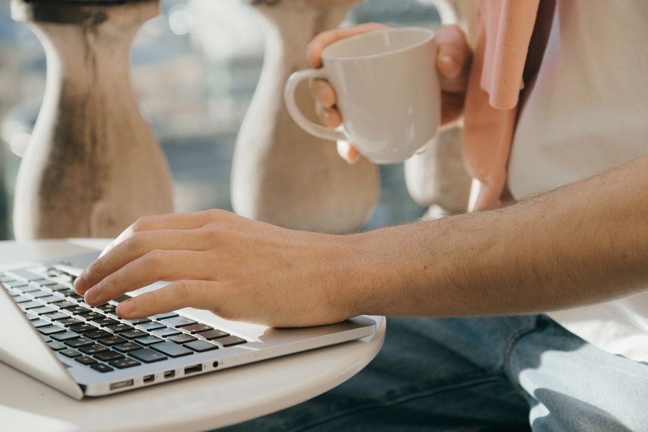 Close-up of a person working outdoors with a laptop and coffee in hand