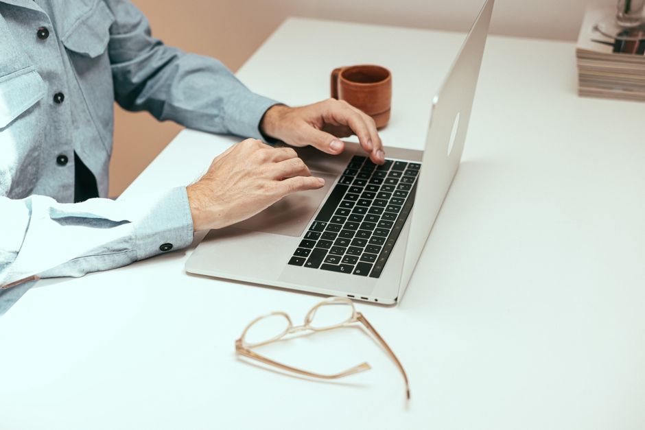 Adult working remotely on laptop with eyeglasses and cup on a white table