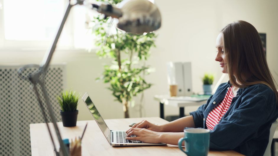 Woman smiling while working on a laptop in a modern office with plants