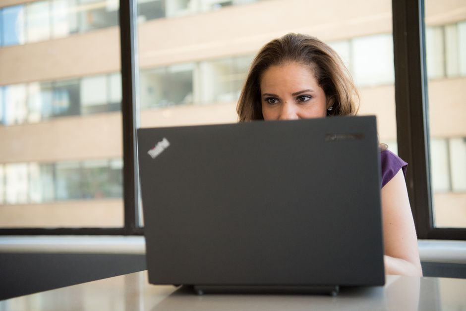 Focused woman using a laptop in a brightly lit office setting, showcasing modern work technology