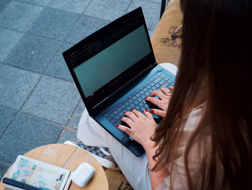Young woman typing on a laptop at an outdoor café, enhancing remote work experience