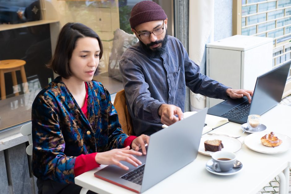 Two adults working on laptops in a cozy café, enjoying coffee and pastries. Perfect for remote work themes